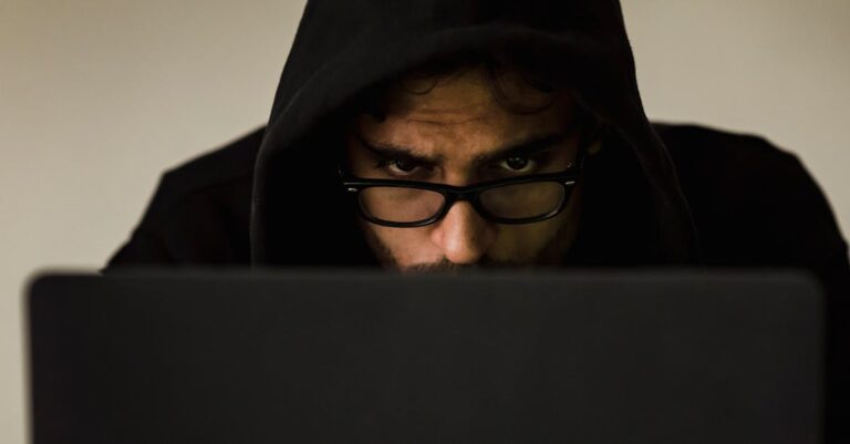 Serious young male programmer wearing black hoodie browsing netbook and hacking software in studio